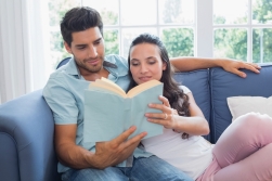 Attractive couple enjoy story book on sofa at home in living room